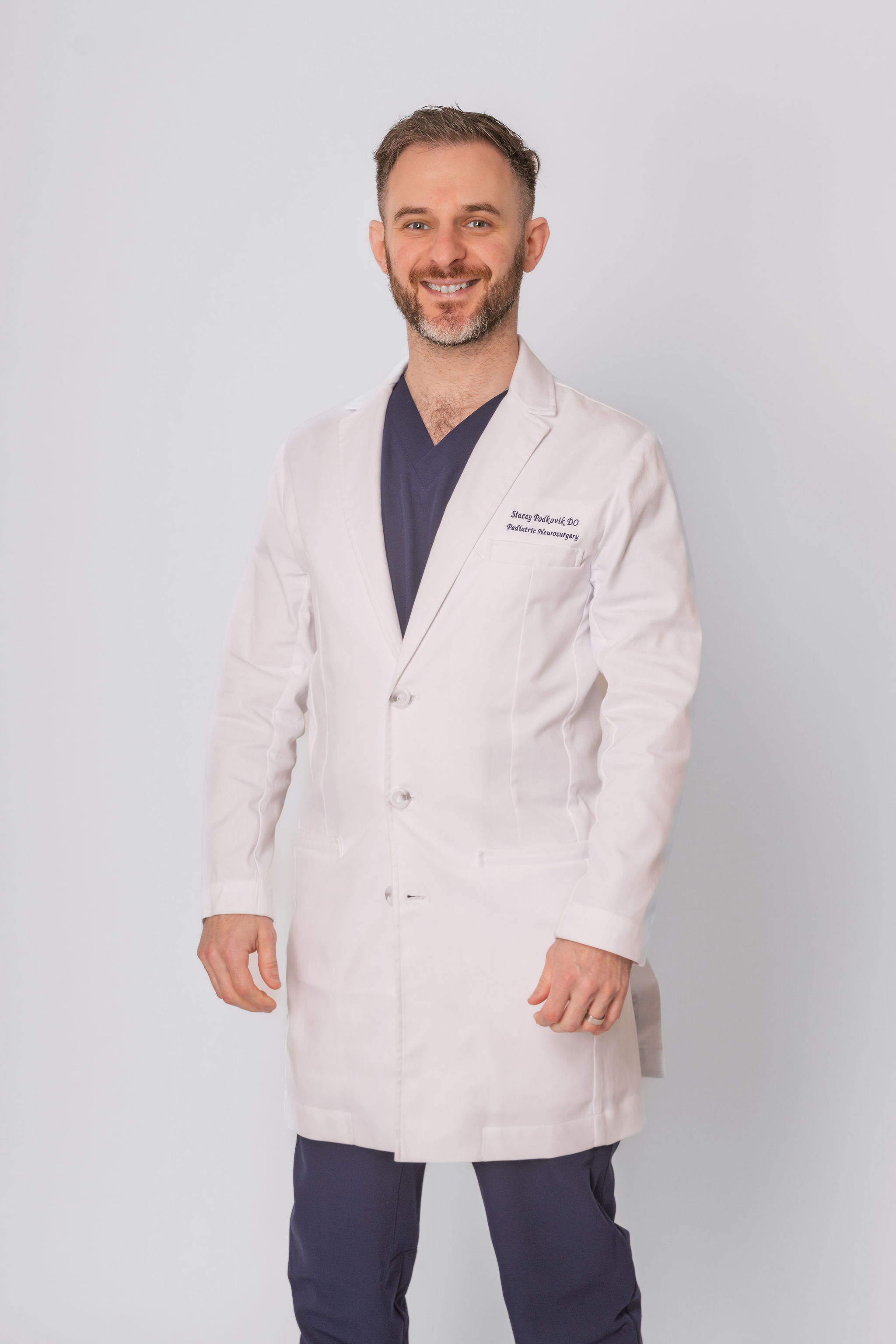 Dr. Stacey Podkovik in his white coat over navy scrubs.