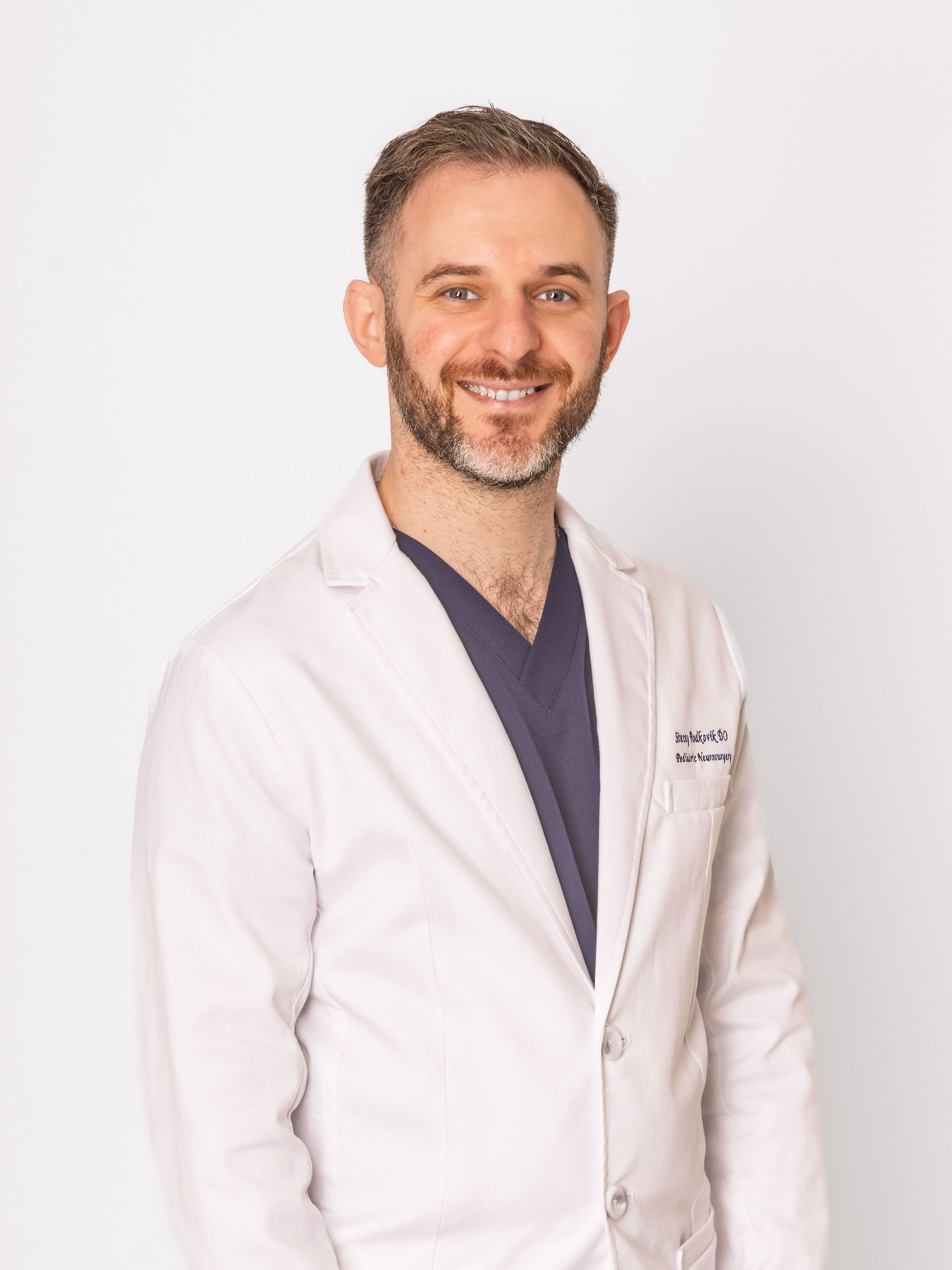 Dr. Stacey in a white coat over navy scrubs.